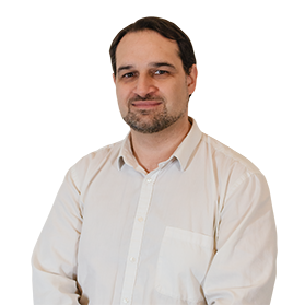Un homme avec les cheveux bruns et une barbe courte, portant une chemise blanche, sourit