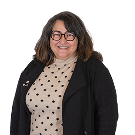 Une femme avec des cheveux bruns mi-longs et des lunettes sourit.